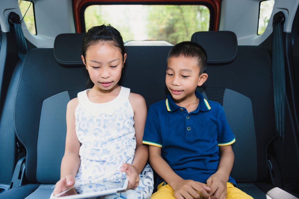 sister and brother watching a movie in the car on a road trip