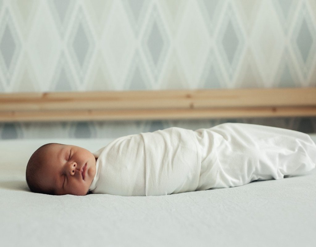 Swaddled sleeping baby in a bed.