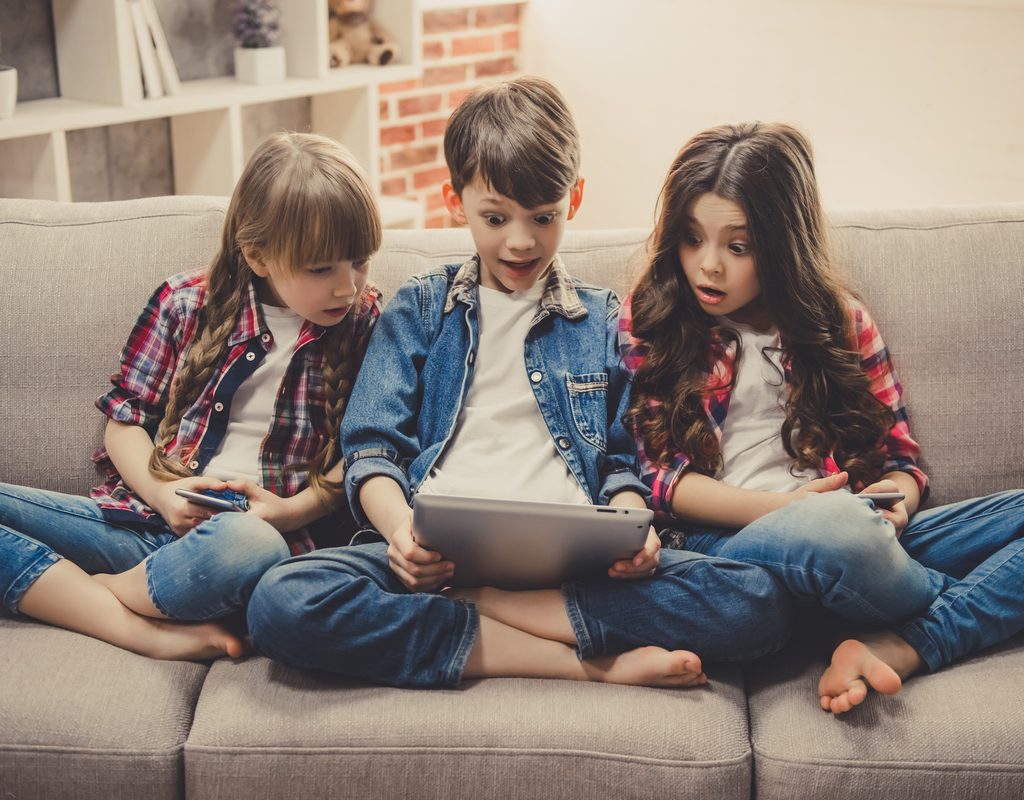 Kids on a couch playing on smart devices.