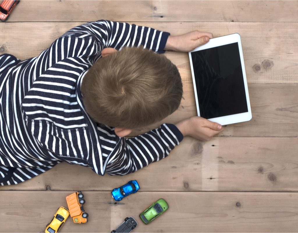 A boy with a tablet and toy cars