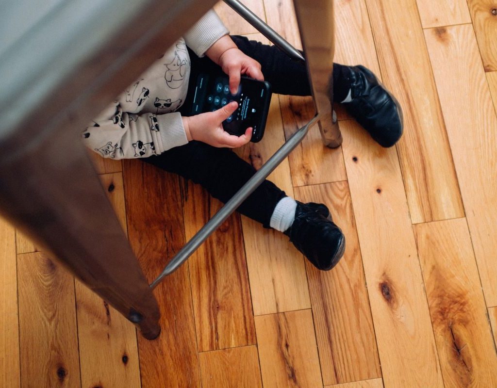 A child under a chair playing with a device