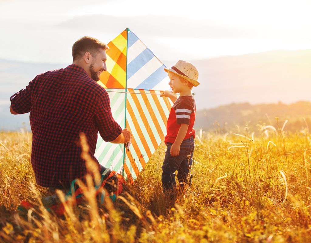 father and son having fun flying a kite in a field