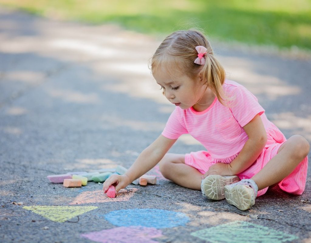 Girl drawing outside with sidewalk chalk