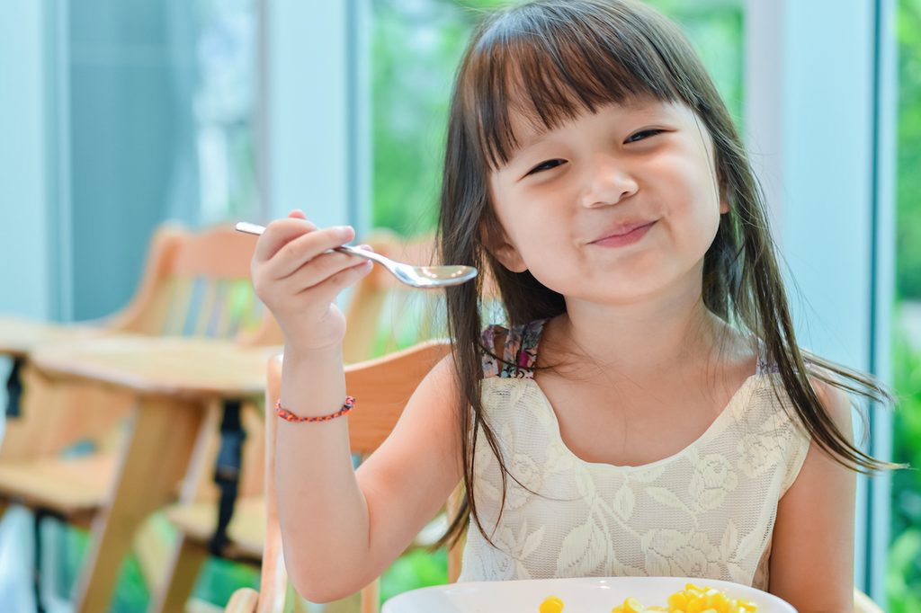A happy girl eating with a spoon