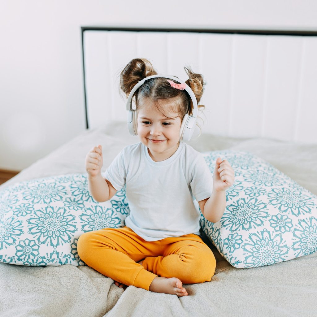 Little girl wearing headphones on a bed