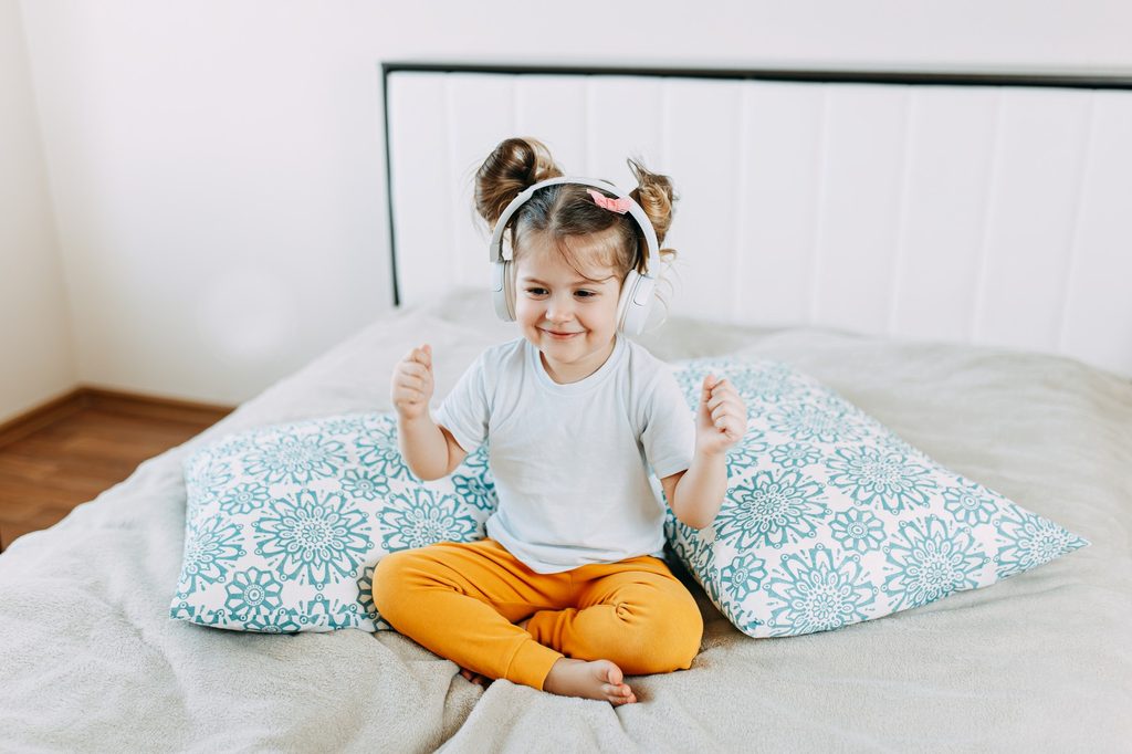 Little girl wearing headphones on a bed