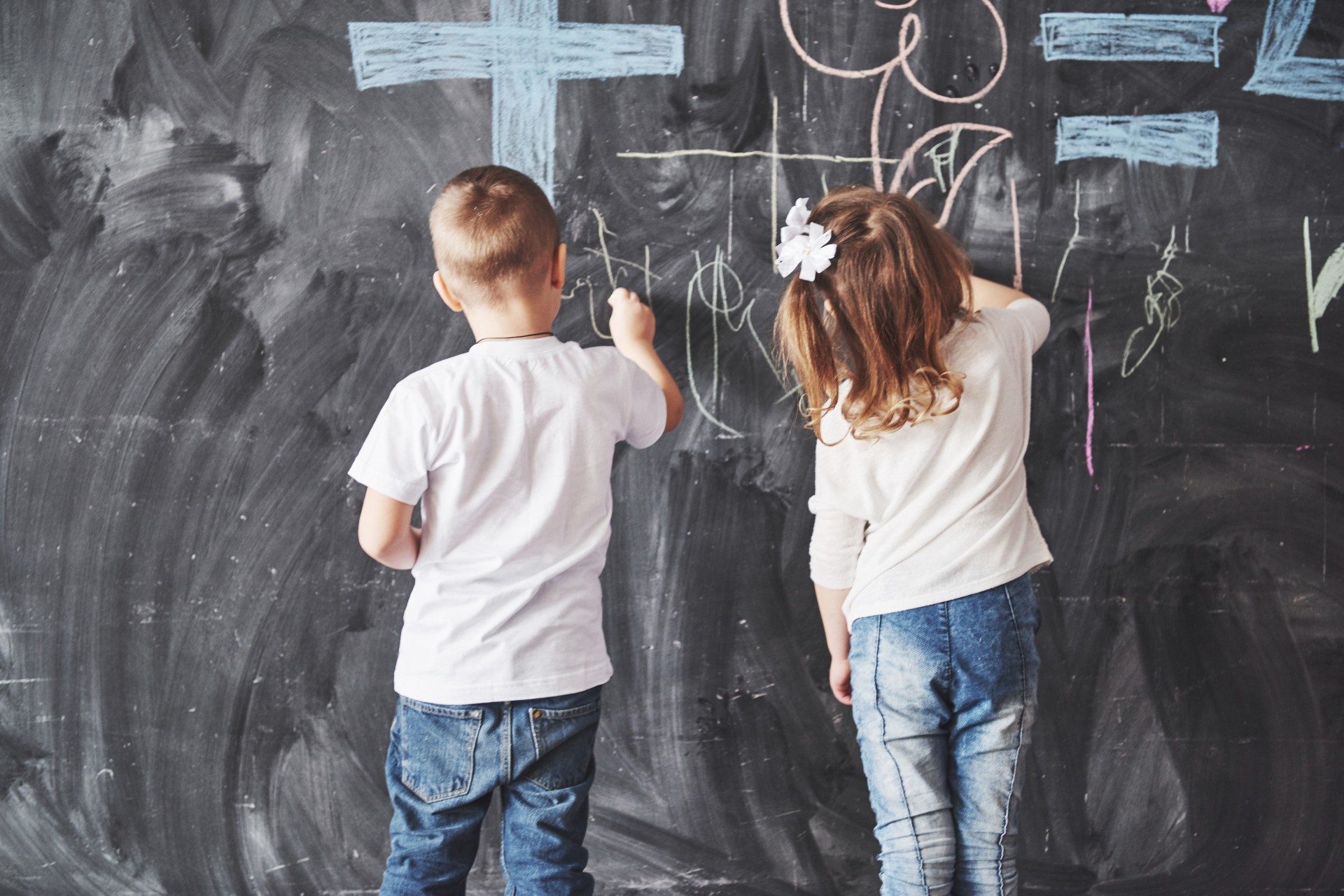 Two kids coloring on a chalkboard wall