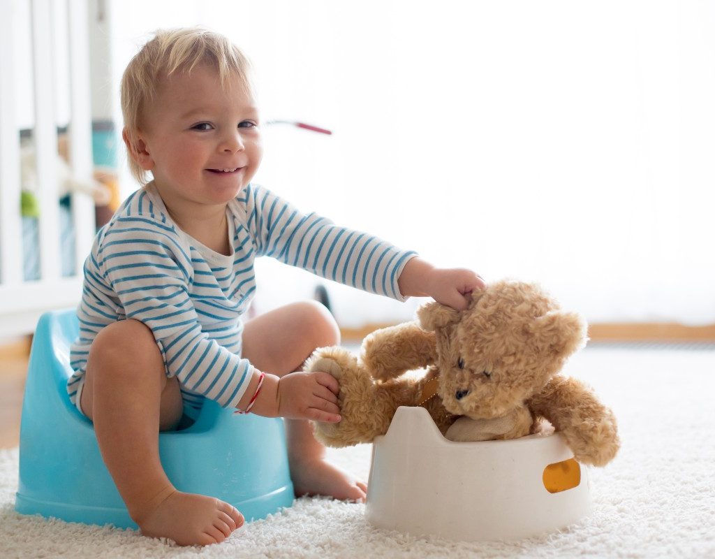 Toddler with stuffed bear on potty training seat.