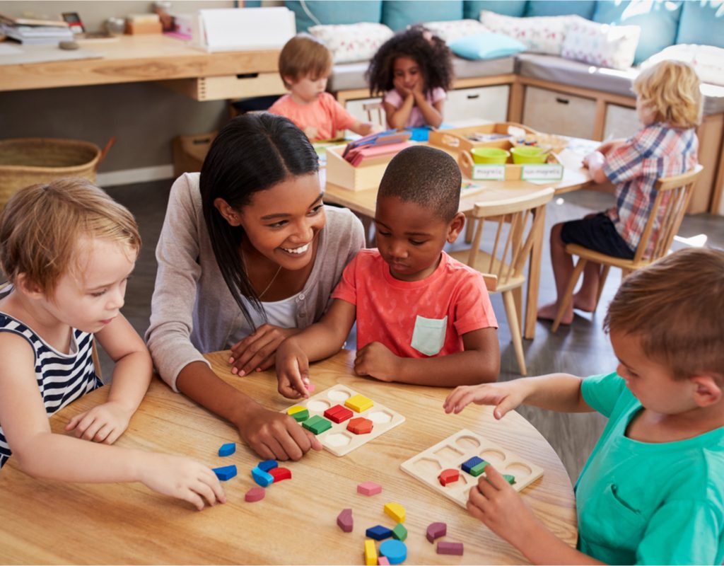 Preschool teacher talking with students at a table.