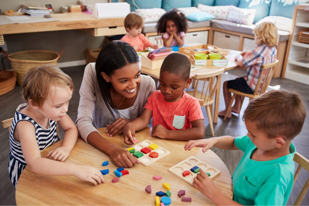 Preschool teacher talking with students at a table.