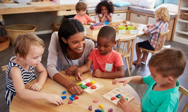 Preschool teacher talking with students at a table.