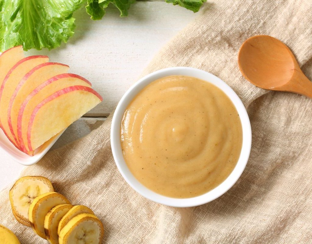 A table with baby food ingredients on it and a bowl of baby food puree