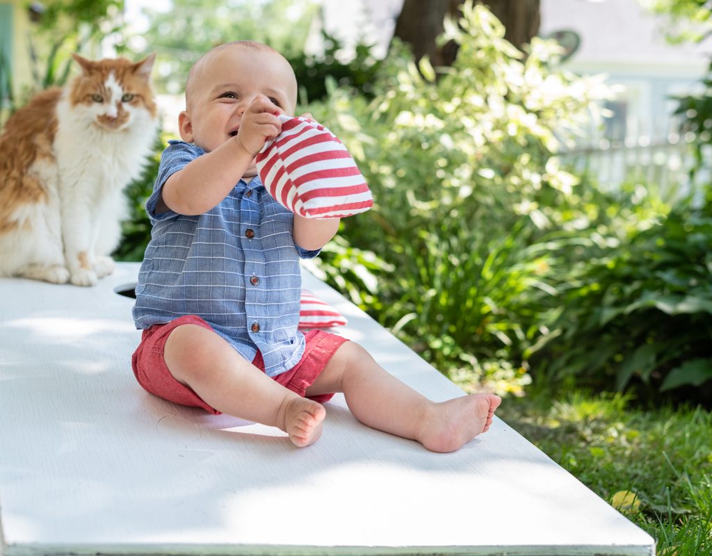 Baby and a cat sitting on a cornhole game