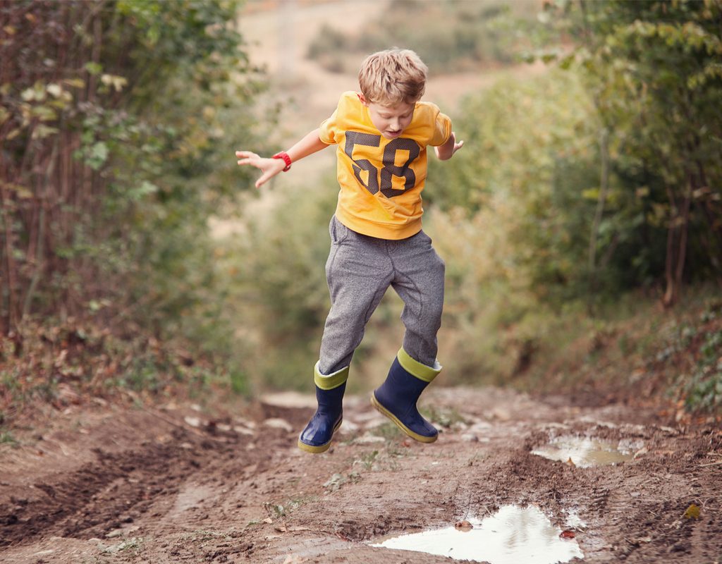 Boy puddle jumping in the woods