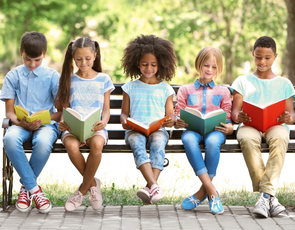 Five kids reading on a bench outside