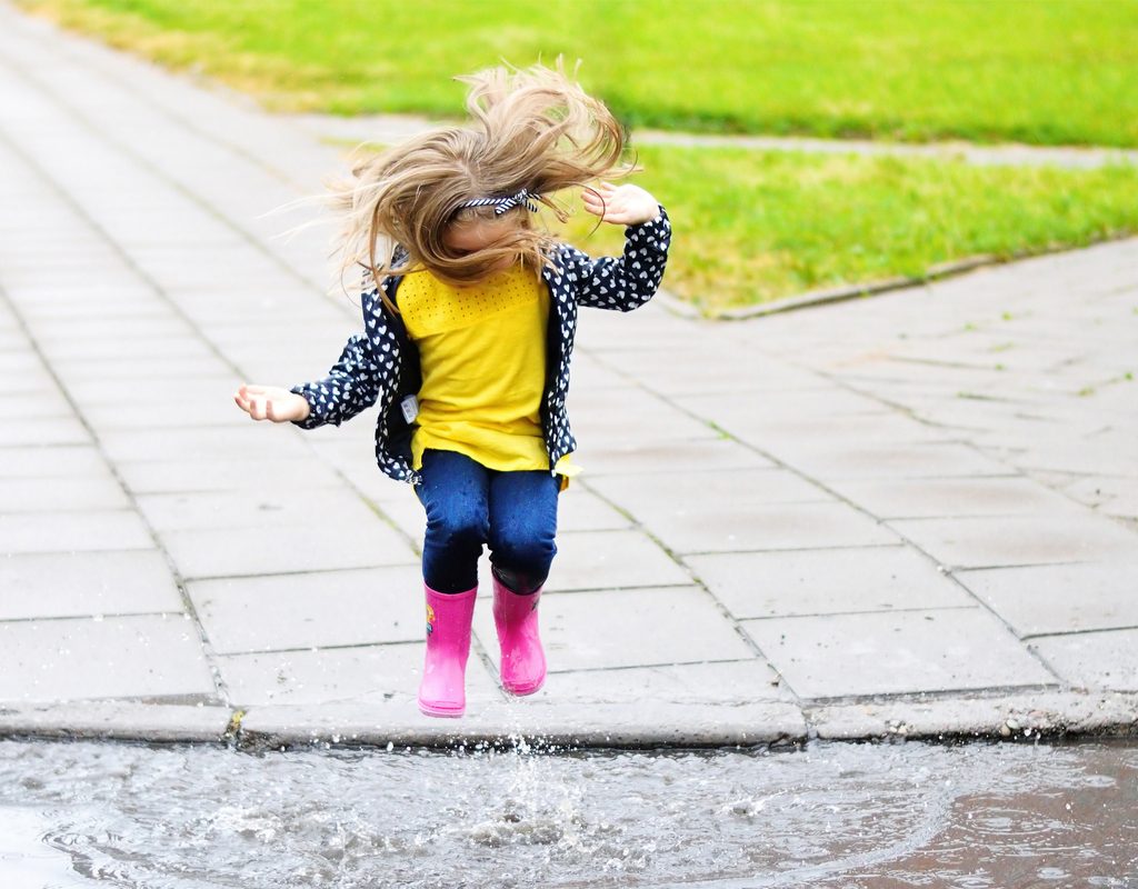 Little girl with rubber boots jumping in a puddle