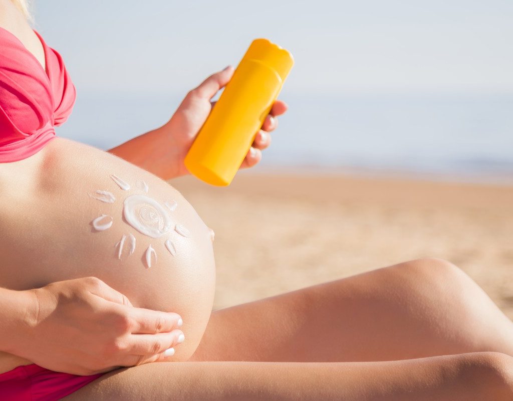 Pregnant woman applying sunscreen to baby bump