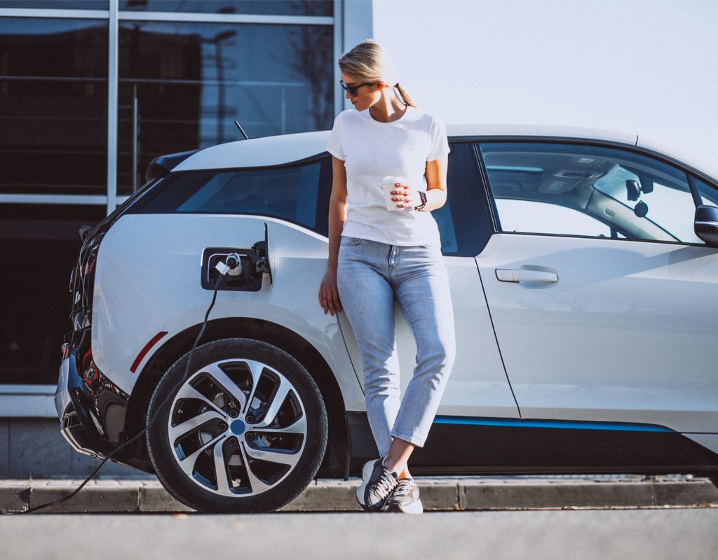 woman standing by with a coffee while her EV charges