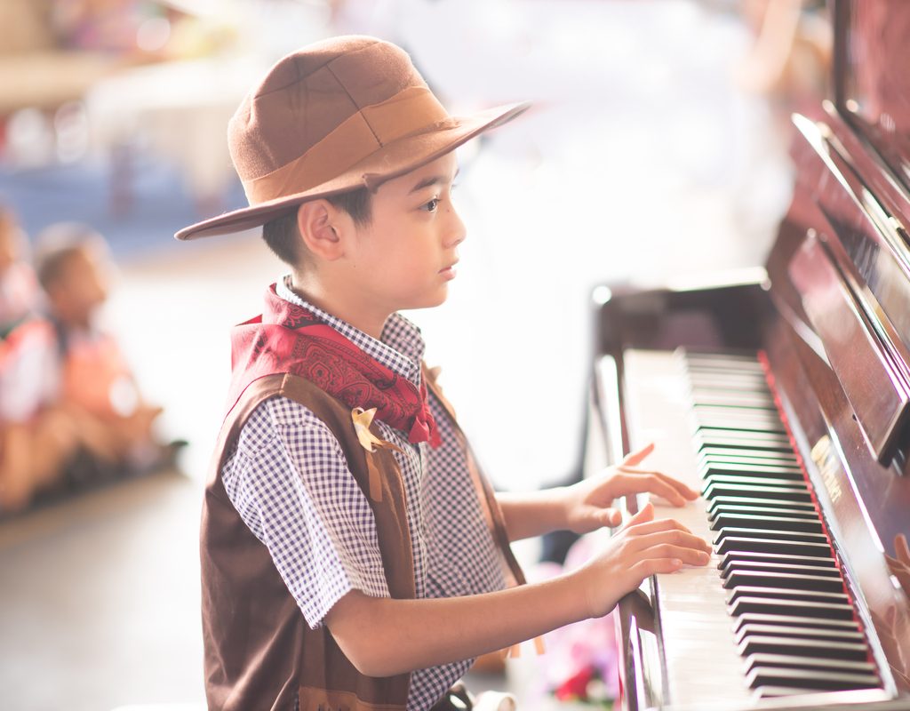 Young boys playing the piano in a talent show wearing a cowboy costume
