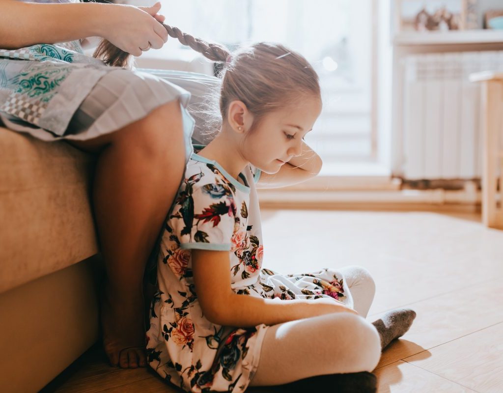 Daughter getting hair braided by her parent