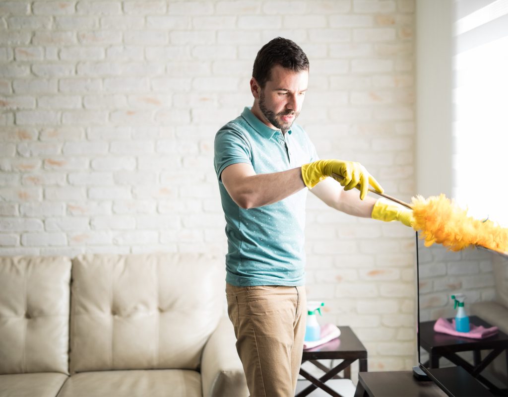 man using duster to clean tv