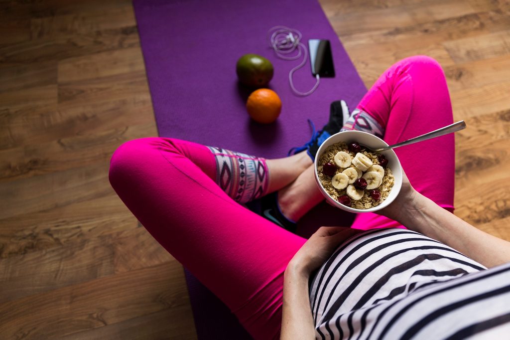 A pregnant woman sitting down eating a bowl of food.