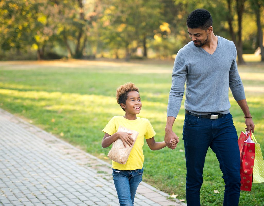 A dad walking with his daughter in the park after shopping.