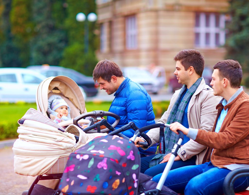 A group of dads hanging out in the city on a park bench.