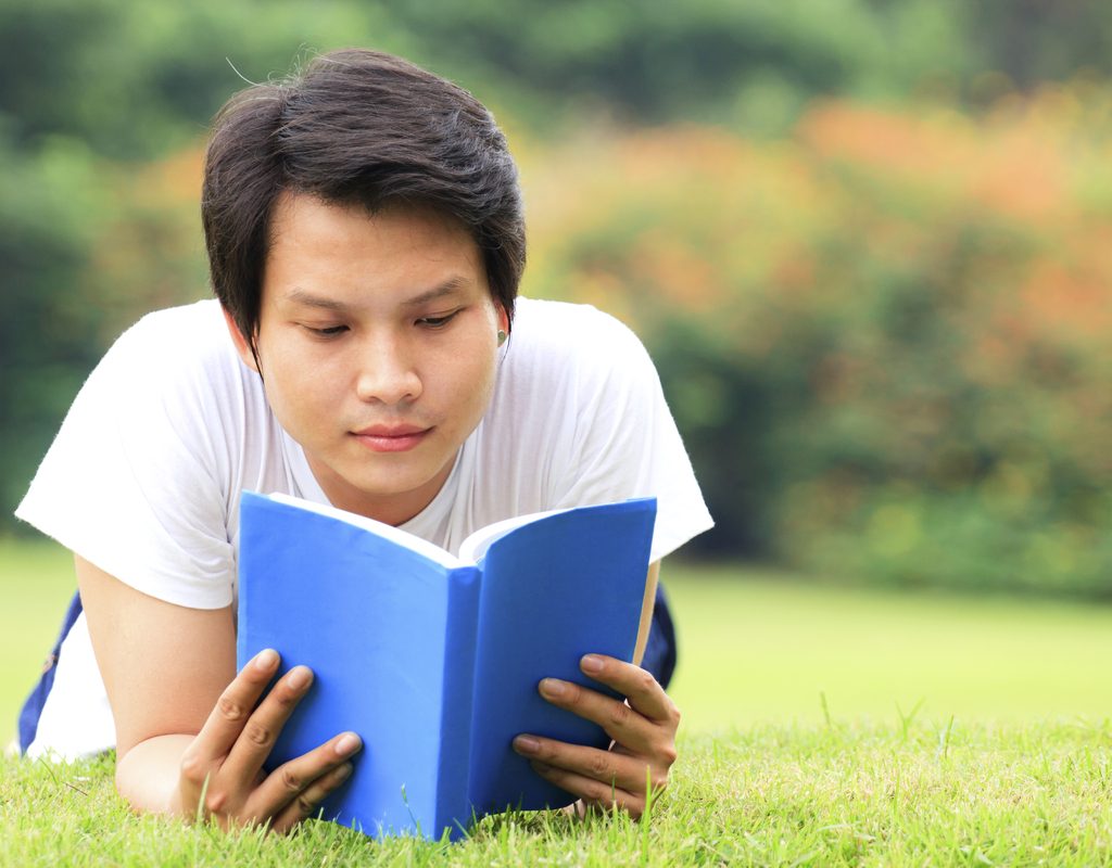 teen boy reading in the grass