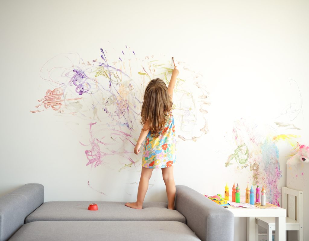 toddler girl getting creative on a wall in the house