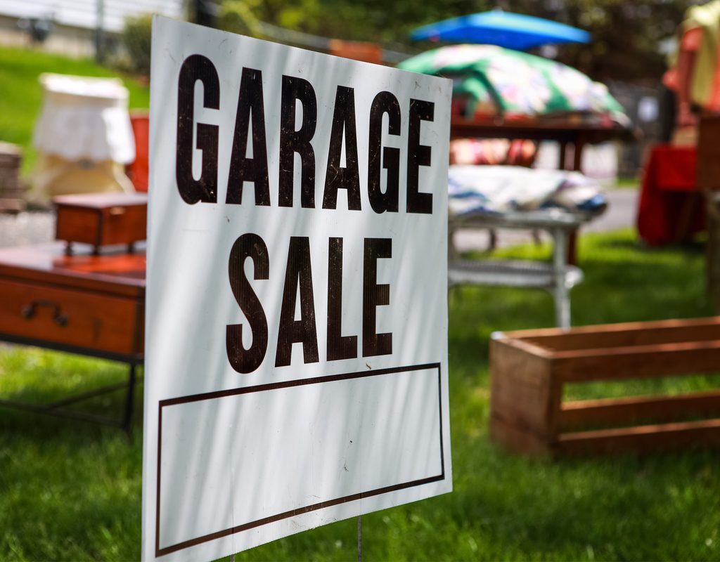 garage sale sign with items for sale behind it