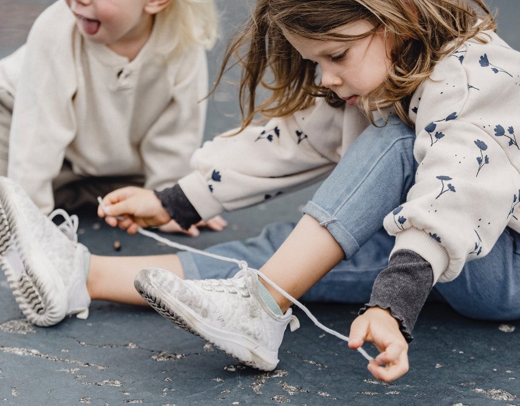 girl showing a friend how to tie her shoes