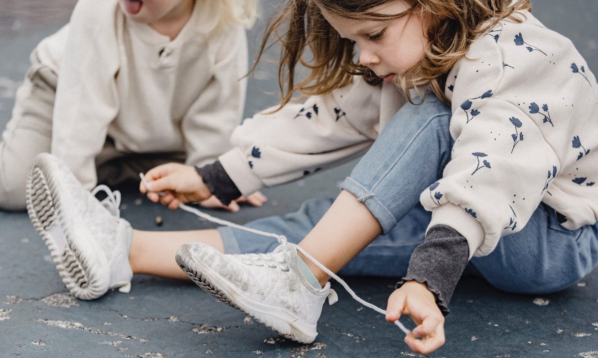 girl showing a friend how to tie her shoes