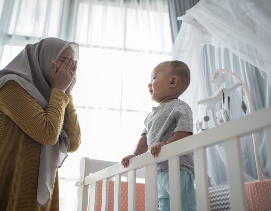 Mom playing peekaboo with son in crib.