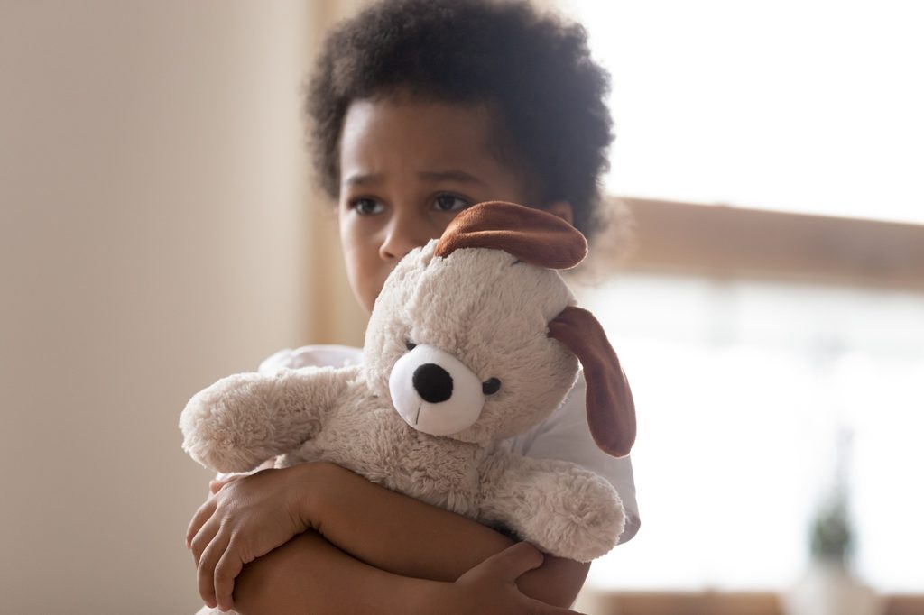 Sad toddler holding a stuffed bear.