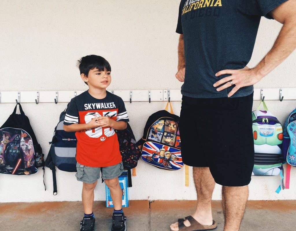 boy standing with adult in hall near backpacks