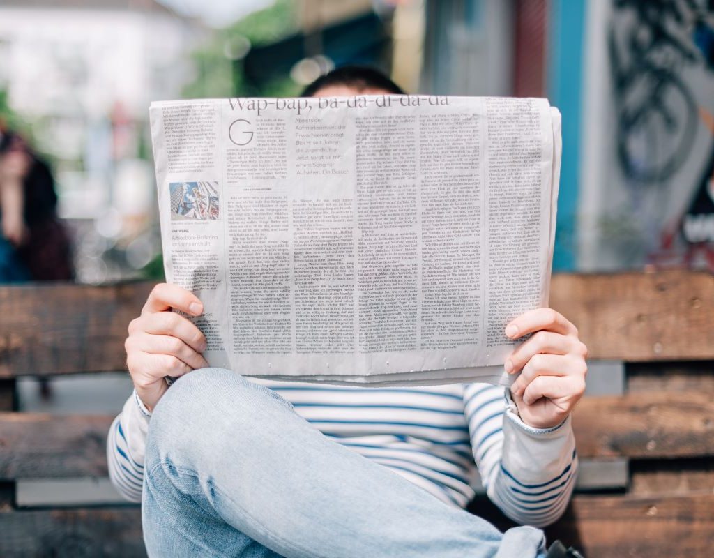 man reading a newspaper sitting on a bench