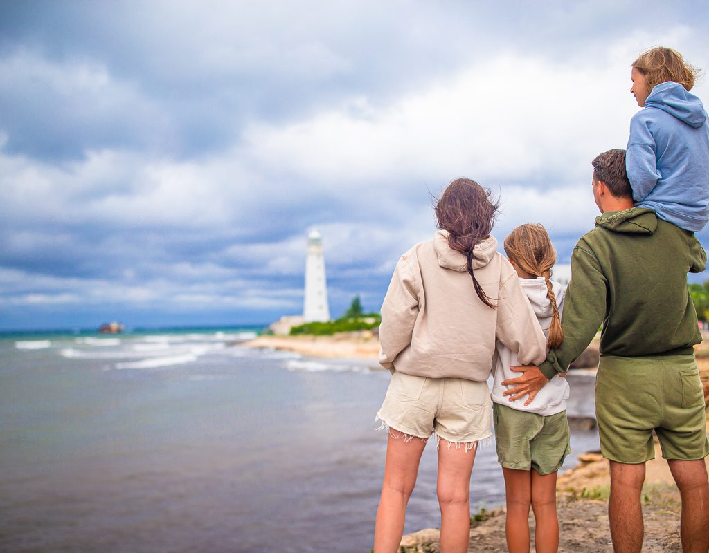 A family standing on the shoreline with a lighthouse in the background.