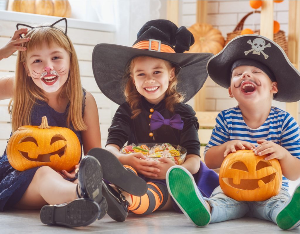 A group of children sitting with Halloween costumes on holding pumpkins.