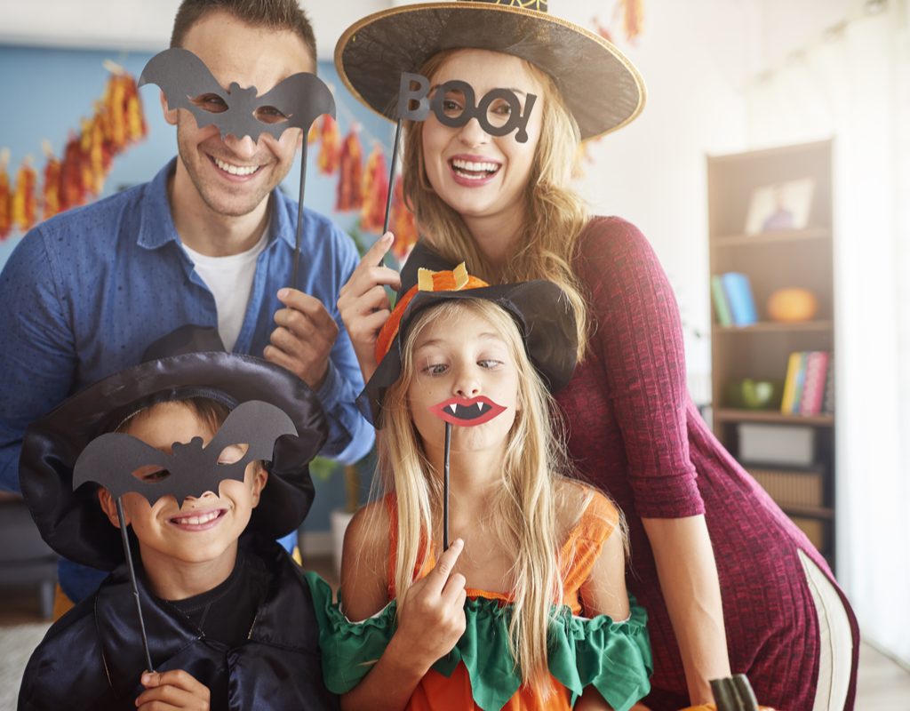 A family taking a cute picture holding Halloween props over their faces.