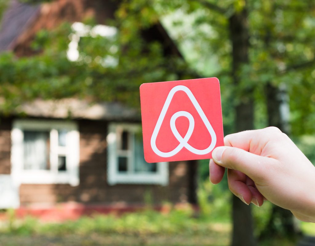 A hand holding an Airbnb sign with a cabin in the background.