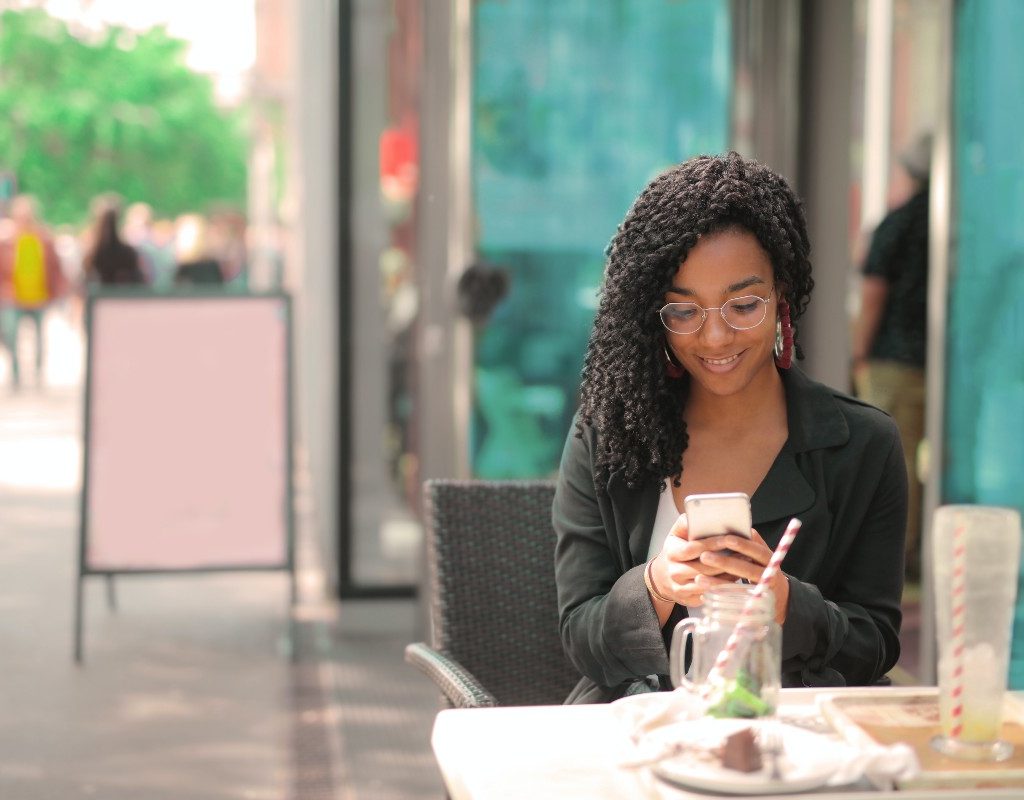 woman looking at her phone while sitting at an outdoor cafe