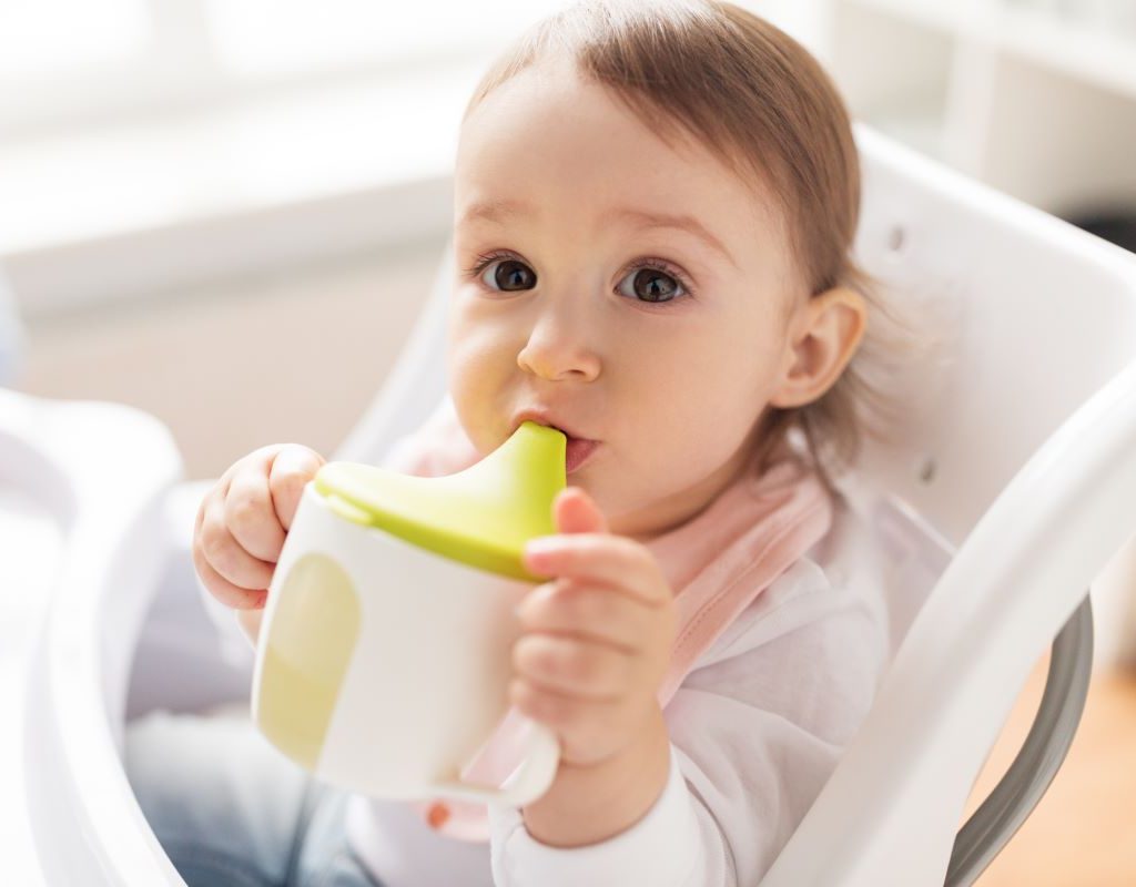 little girl drinking from a sippy cup in a highchair