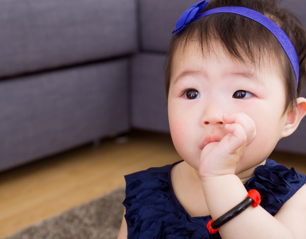 Baby girl with blue headband sucking on her thumb