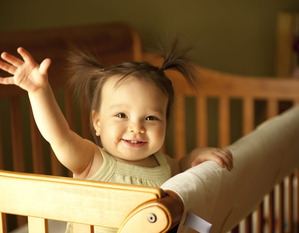 Baby girl standing and waving in crib