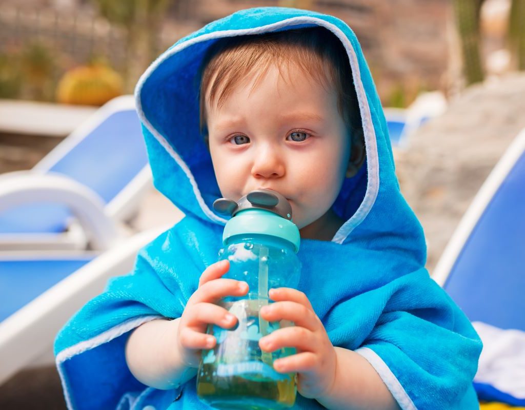 Little boy wearing a blue towel and drinking from a sippy cup