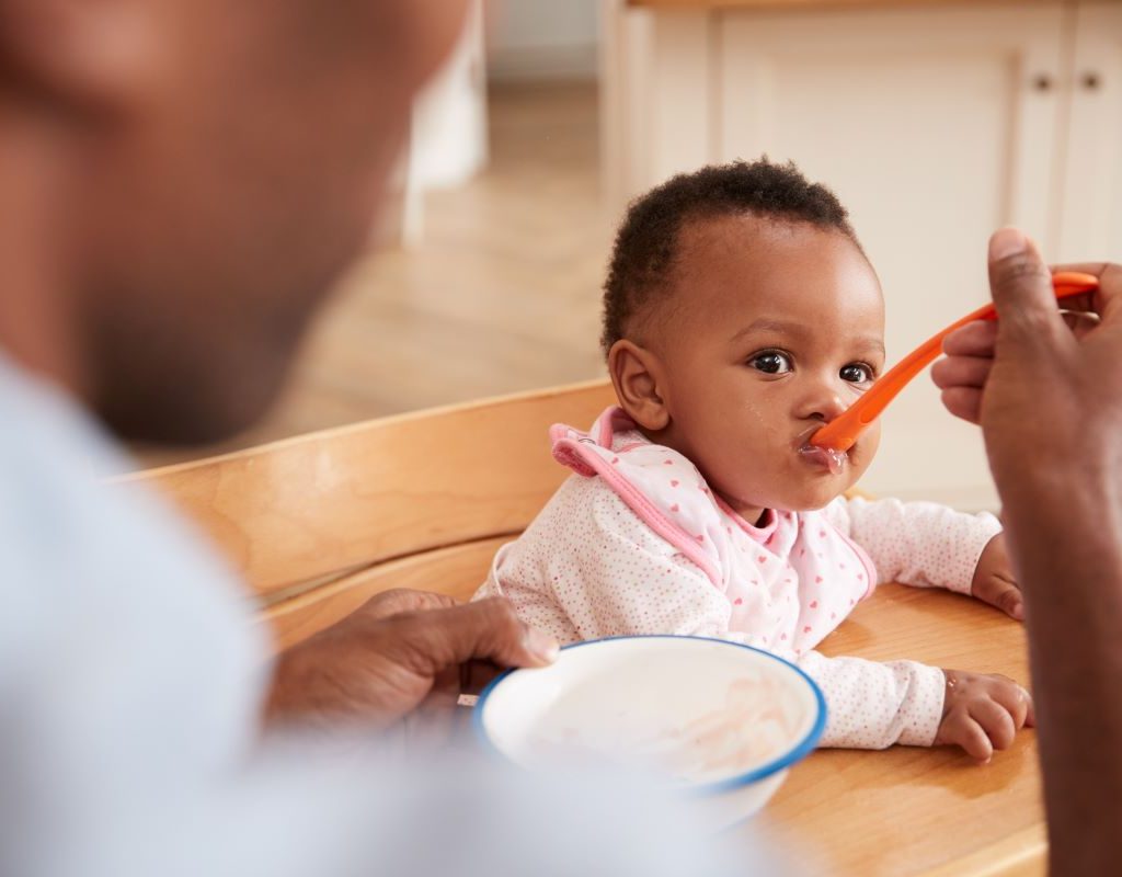 Dad spoon feeds baby in highchair.