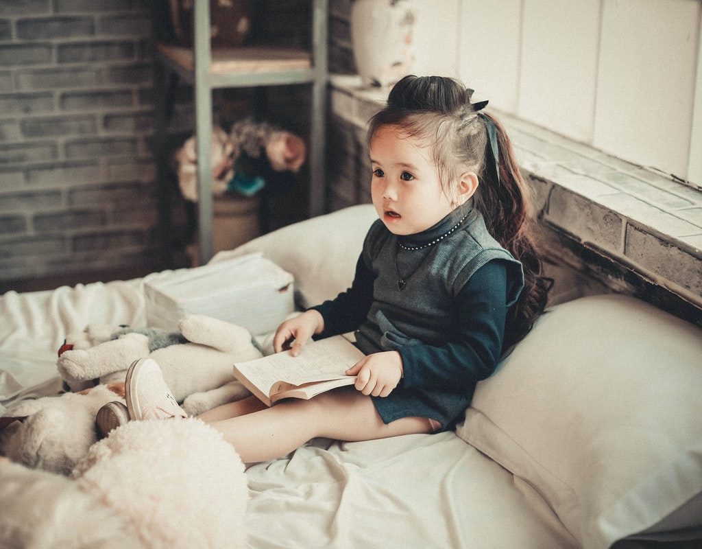 Little girl sitting up in bed with a book