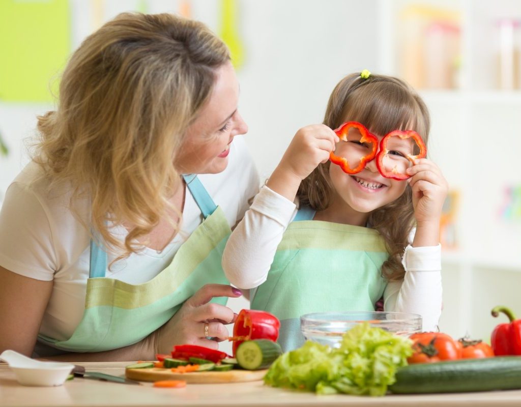 A mother and daughter cooking in the kitchen, with the child holding pepper slices up to her eyes