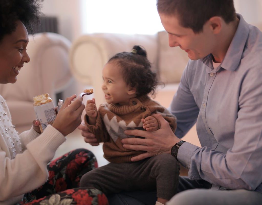 Dad holding daughter on lap while Mom feeds her